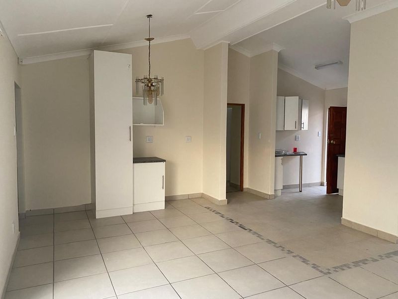 An open-plan living and kitchen area featuring neutral tiled flooring, built-in cabinetry, and a coved ceiling, offering a versatile blank canvas.