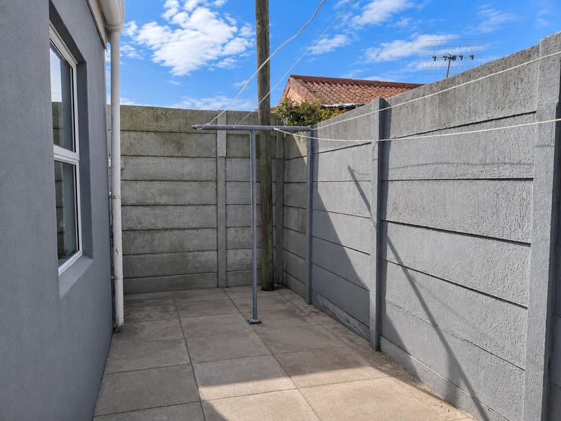 A paved rear courtyard area featuring a precast concrete boundary wall and a fixed washing line installation.