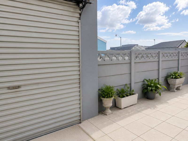 A clean, tiled outdoor patio area featuring a secure roller shutter door and a decorative precast concrete boundary wall.