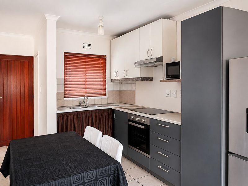 A functional kitchen featuring modern grey and white cabinetry, integrated appliances, a tiled backsplash, and a double sink with a window view.