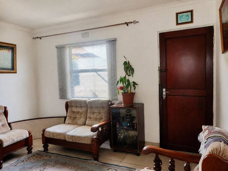 A living room featuring tiled flooring, a timber door, and a window fitted with venetian blinds.