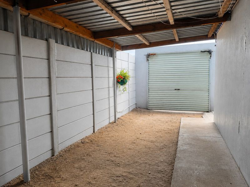 A covered garage space featuring precast concrete walls, a roller shutter door, and an unpaved dirt floor.