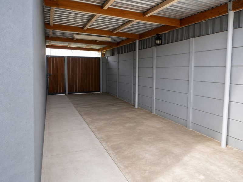 A clean, covered carport or garage area featuring a corrugated metal roof, timber beams, and secure precast concrete walling with a gated entrance.