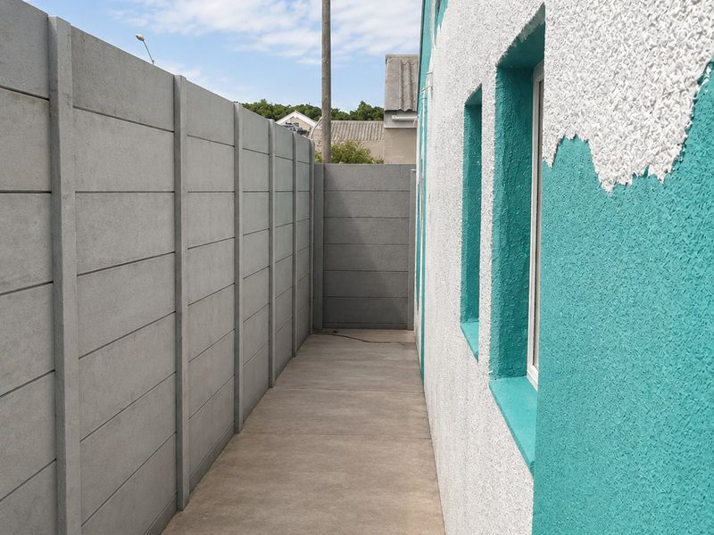 A side passage featuring a concrete pathway bordered by a precast concrete boundary wall and the exterior wall of the house.