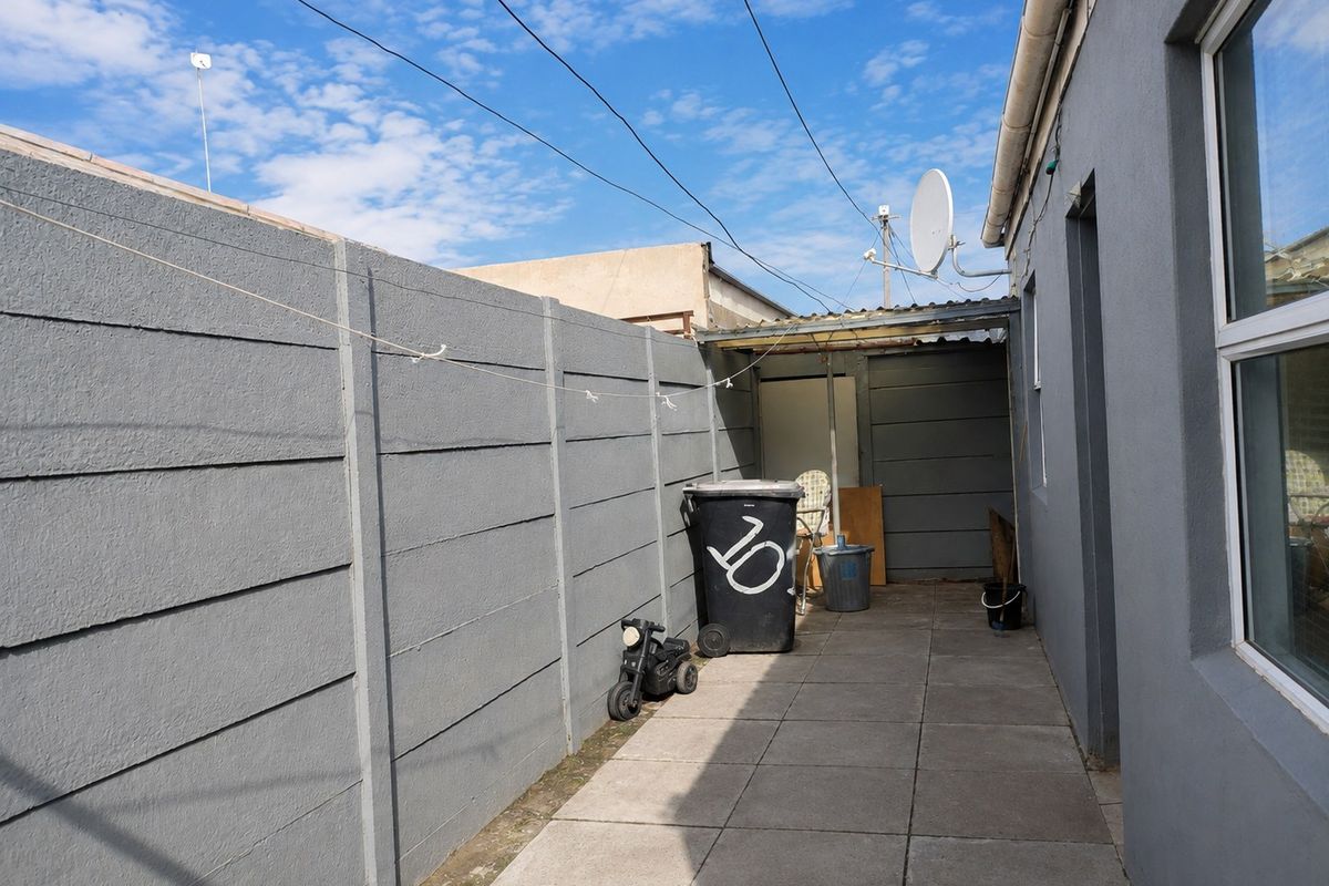 A narrow paved side or rear walkway featuring a precast concrete boundary wall and a small covered utility area.