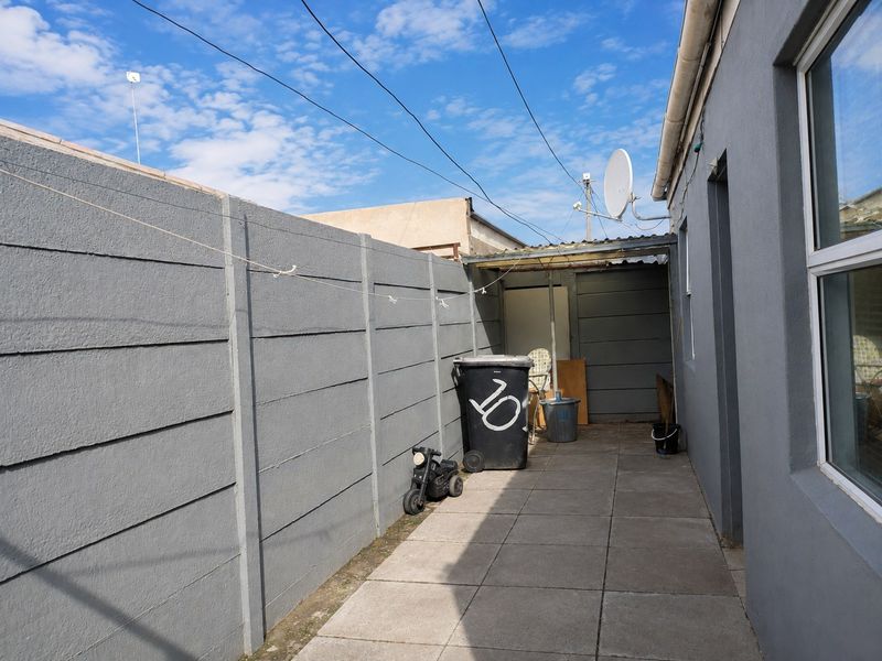 A narrow paved side or rear walkway featuring a precast concrete boundary wall and a small covered utility area.