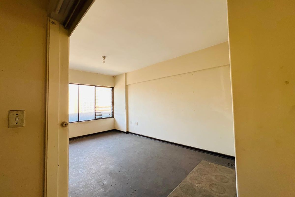 An empty, dated bedroom featuring plain walls, worn flooring, and an aluminium-framed window, offering a blank canvas for renovation.