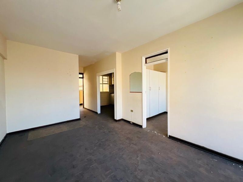 An empty living area featuring neutral walls, dark flooring, and access to adjacent rooms with built-in storage cupboards.