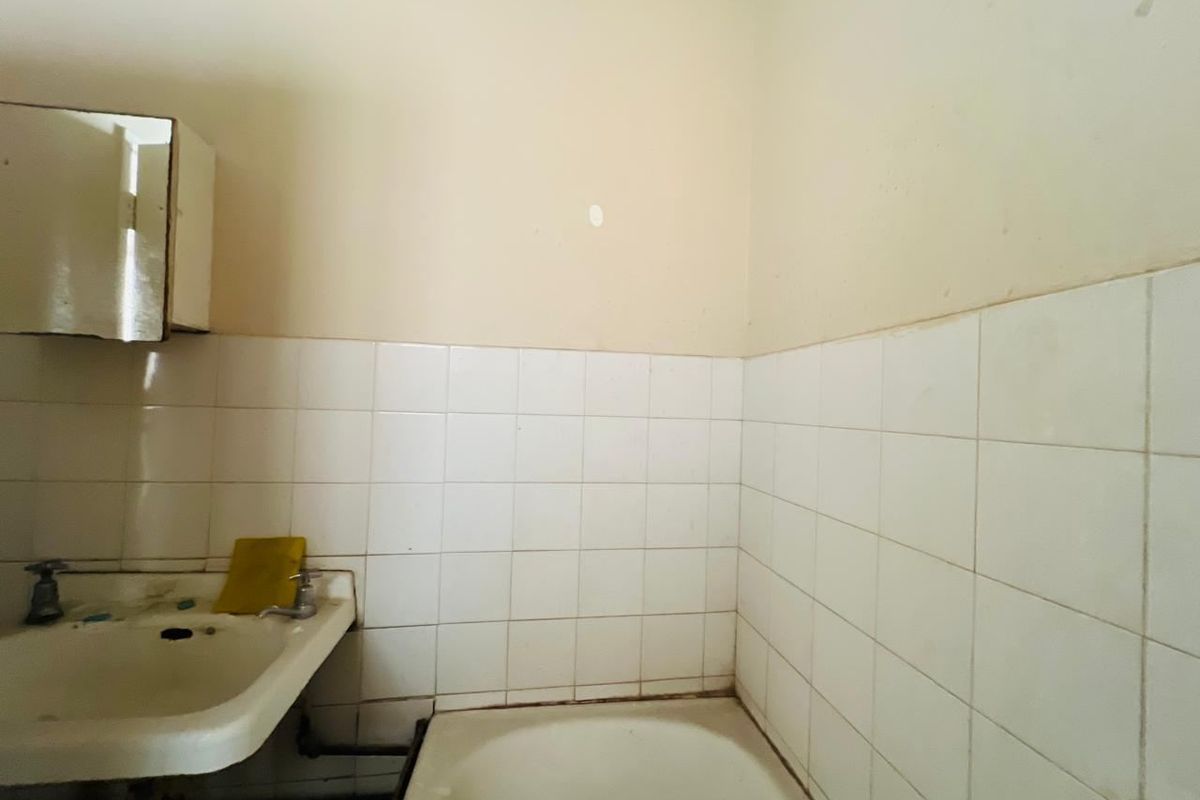 A dated bathroom featuring a wall-mounted basin, bathtub, and tiled splashback, requiring renovation to update the finishes and fixtures.
