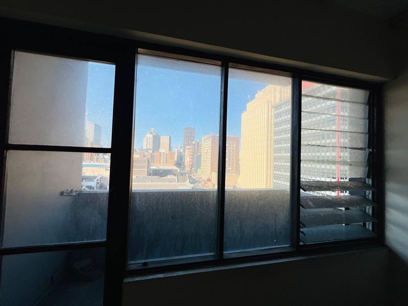 A view of the city skyline captured through large metal-framed windows with integrated louvre sections.