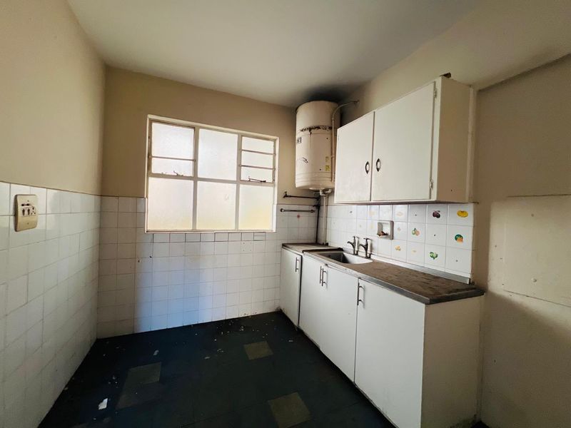 A dated kitchen featuring basic built-in cabinetry, a stainless steel sink, and tiled splashbacks, requiring renovation to modernize the space.