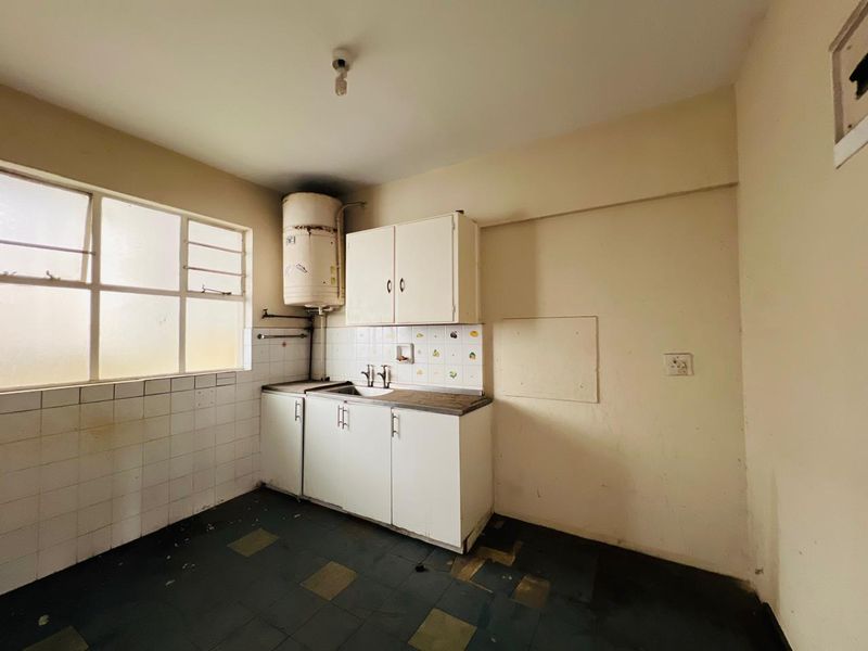 A dated, empty kitchen featuring basic built-in cabinetry, a sink, and a wall-mounted electric water heater, requiring significant renovation and cosmetic updates.