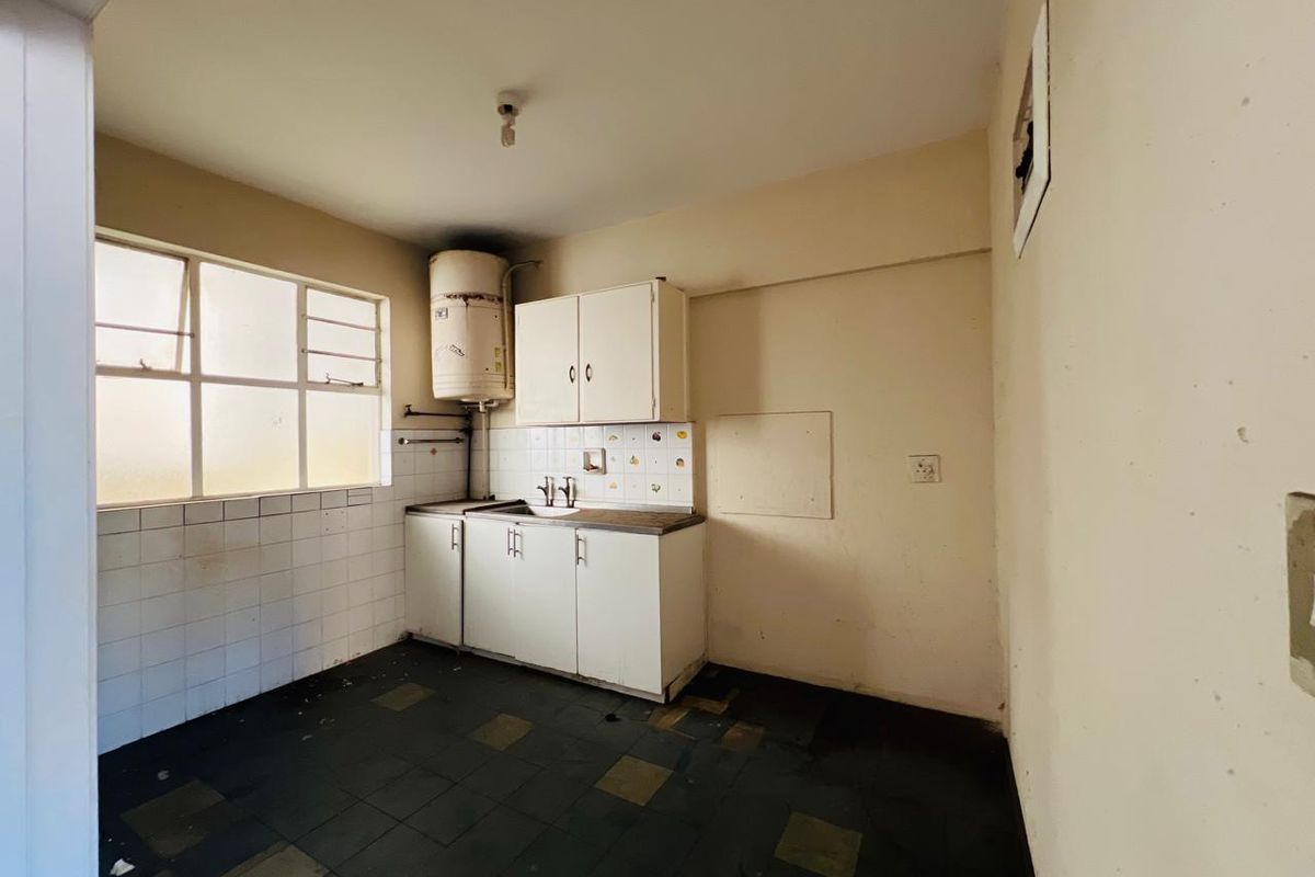 A dated, empty kitchen featuring basic cabinetry, a sink, and tiled flooring, requiring renovation to modernize the space.