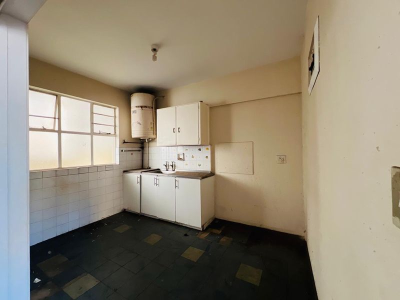 A dated, empty kitchen featuring basic cabinetry, a sink, and tiled flooring, requiring renovation to modernize the space.