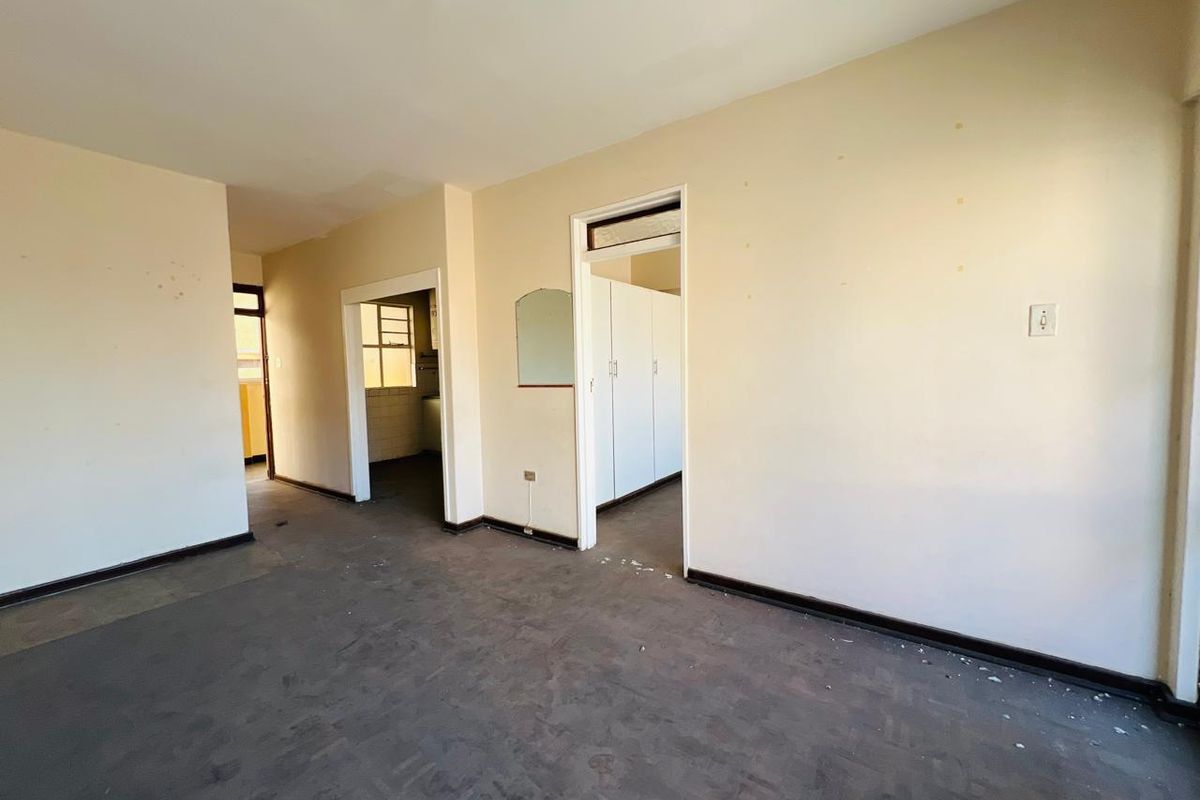 An empty living area featuring original parquet flooring and built-in cupboards, offering a blank canvas for renovation and interior design updates.