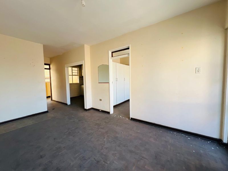 An empty living area featuring original parquet flooring and built-in cupboards, offering a blank canvas for renovation and interior design updates.