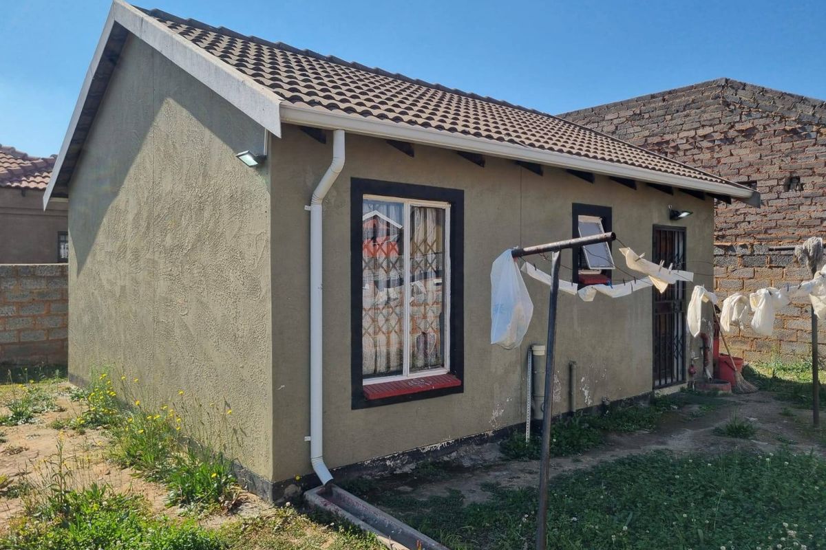 Rear view of a small residential structure featuring a tiled roof, plastered exterior walls, and security bars on windows and doors.