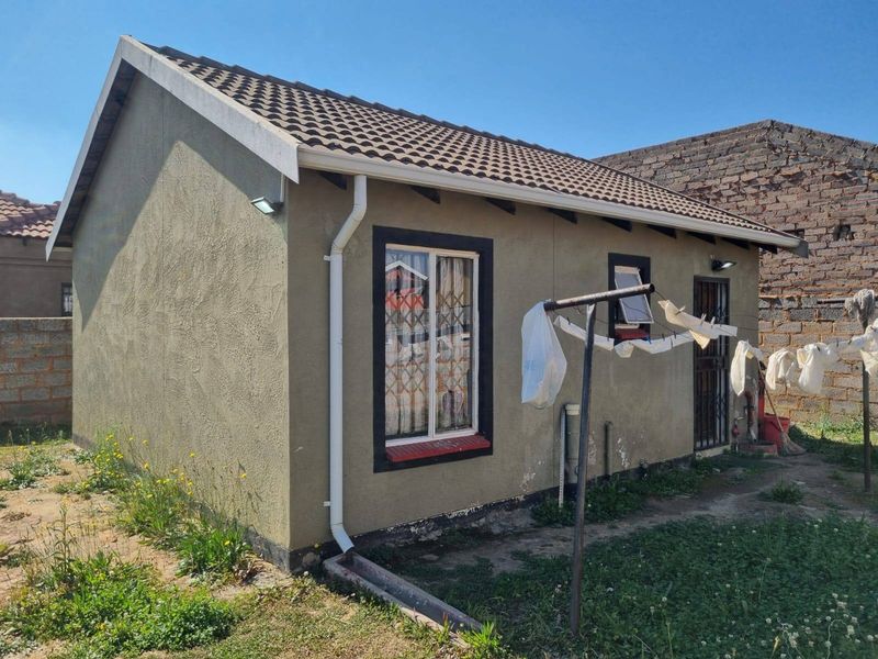 Rear view of a small residential structure featuring a tiled roof, plastered exterior walls, and security bars on windows and doors.