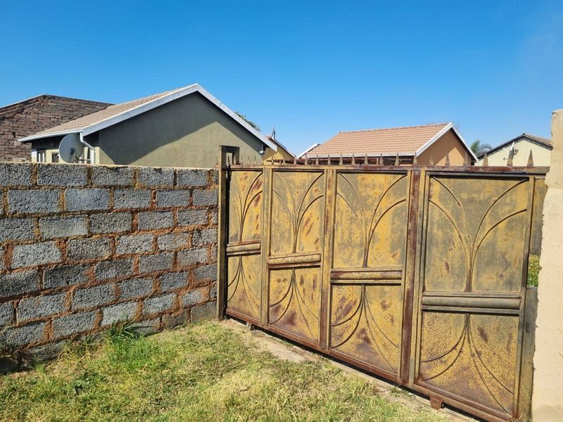 Exterior view showing a metal sliding gate and an unfinished concrete block boundary wall.
