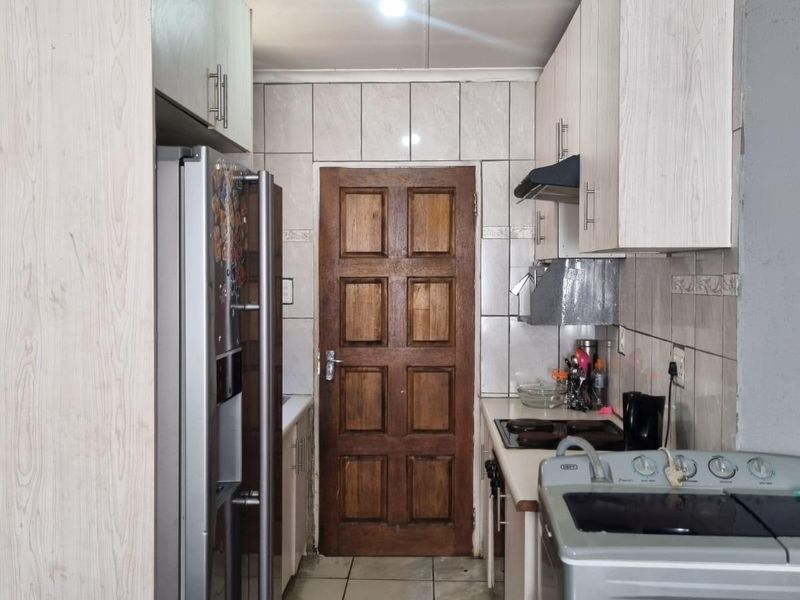 A compact kitchen featuring light-toned built-in cabinetry, tiled backsplash, and tiled flooring, providing a functional layout with essential cooking infrastructure.