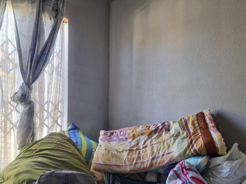 A bedroom space featuring a window with a security gate, requiring cosmetic updates and wall repairs to improve the overall condition.