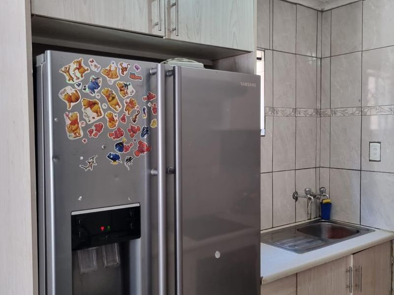 A functional kitchen area featuring light wood-grain cabinetry, a stainless steel sink, and tiled wall finishes.