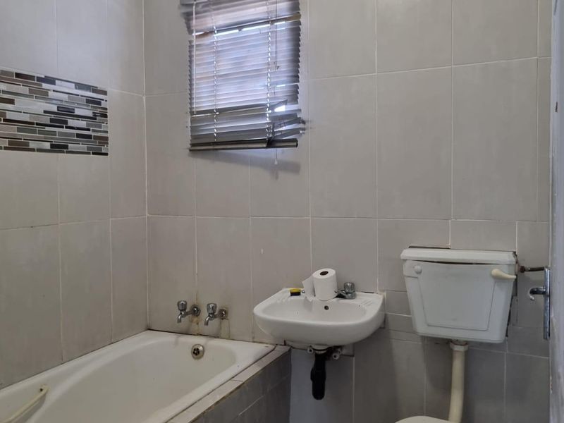 A functional bathroom featuring a bathtub, wall-mounted basin, and toilet, finished with neutral wall and floor tiling.