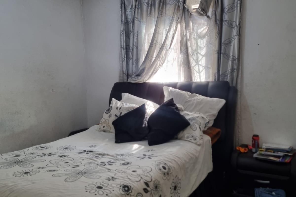 A bedroom featuring a window with curtains and a ceiling light fixture, showing signs of wear on the wall surfaces.