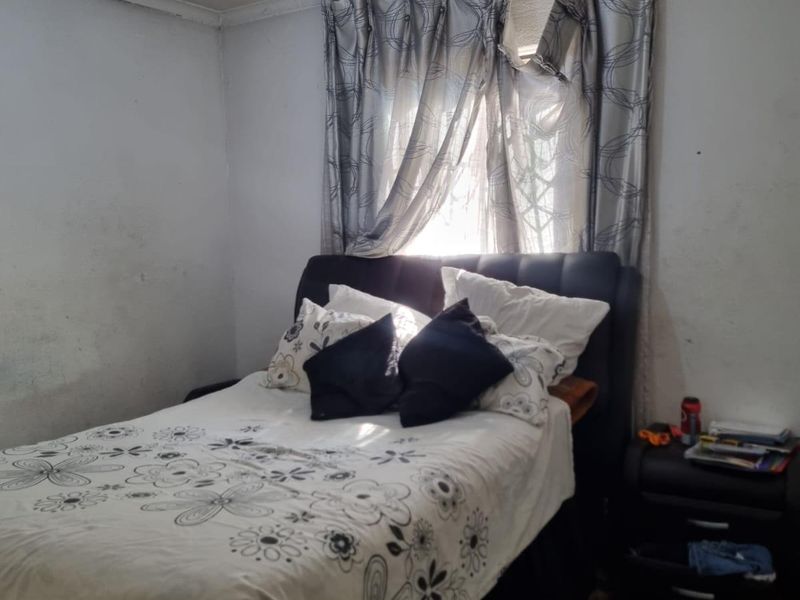 A bedroom featuring a window with curtains and a ceiling light fixture, showing signs of wear on the wall surfaces.