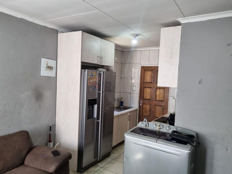A compact kitchen area featuring built-in cabinetry, tiled splashbacks, and tiled flooring, requiring cosmetic updates to improve the overall aesthetic and finish.