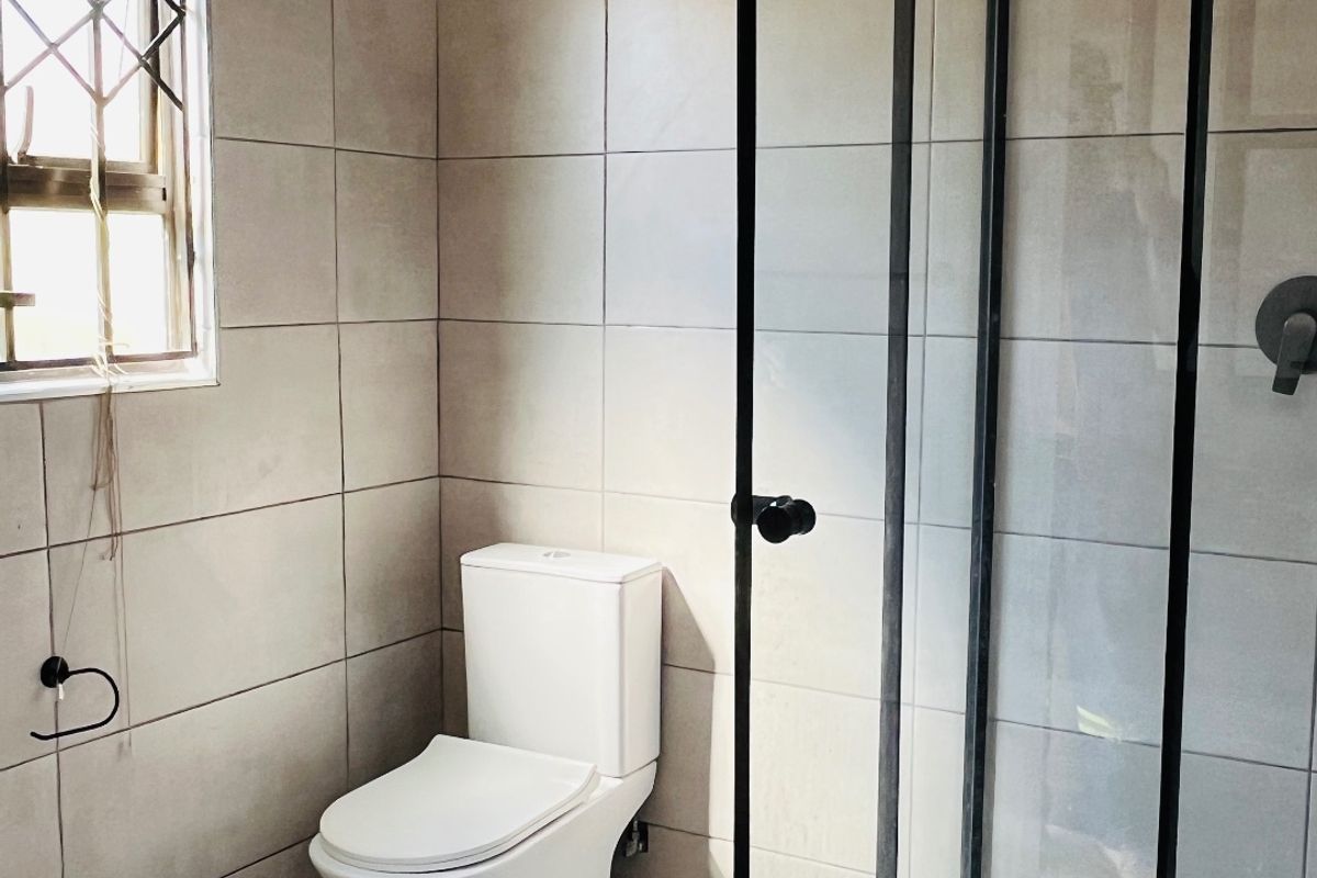 A clean, modern bathroom featuring a glass-enclosed shower, neutral wall and floor tiling, and a standard toilet.