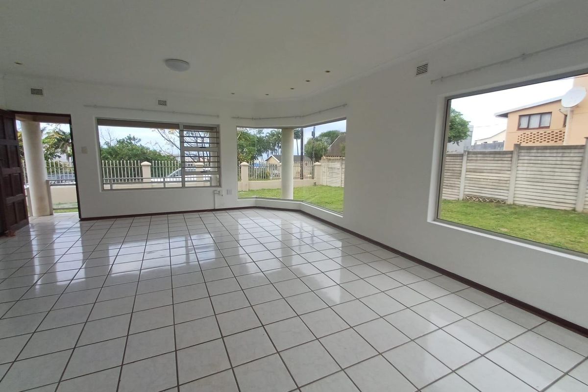 A bright, spacious, and empty living room featuring large windows, tiled flooring, and direct access to the outdoor garden area.