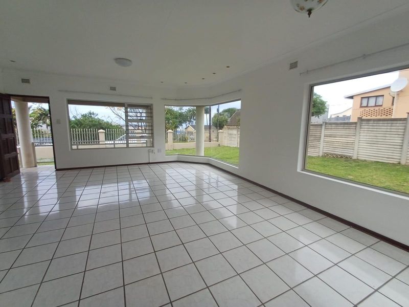 A bright, spacious, and empty living room featuring large windows, tiled flooring, and direct access to the outdoor garden area.