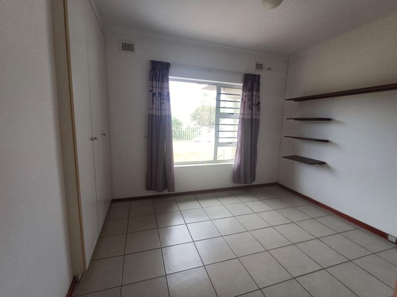 A clean, empty bedroom featuring tiled flooring, built-in cupboards, and wall-mounted shelving, offering a neutral space ready for personalization.