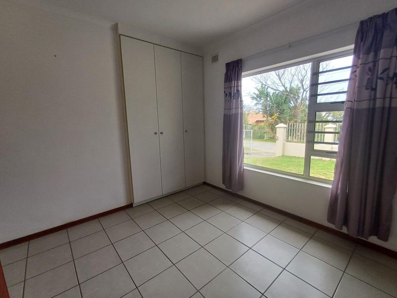 A bright, empty bedroom featuring neutral tiled flooring and built-in cupboards, offering a clean and versatile space ready for personalization.