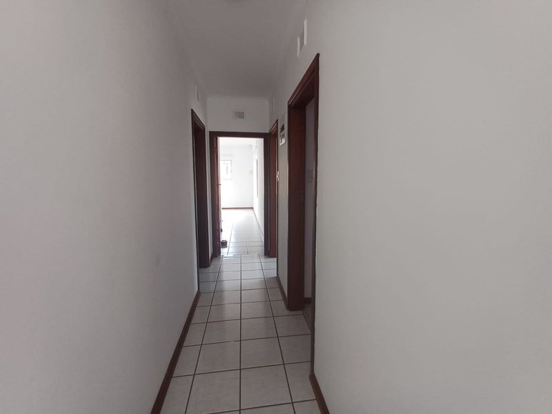 A clean, empty hallway featuring neutral tiled flooring and wooden door frames, providing access to multiple rooms within the home.