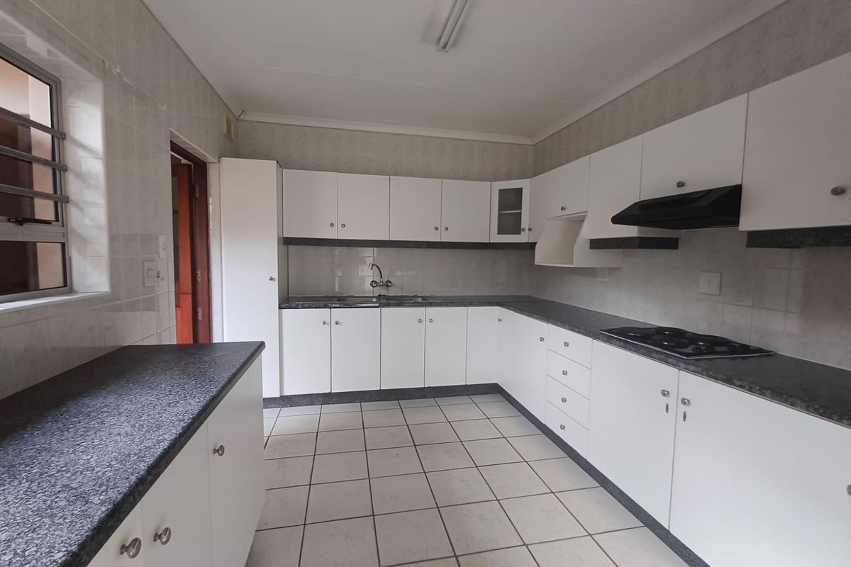 A functional, empty kitchen featuring white cabinetry, dark laminate countertops, a built-in hob with extractor fan, and neutral tiled flooring.