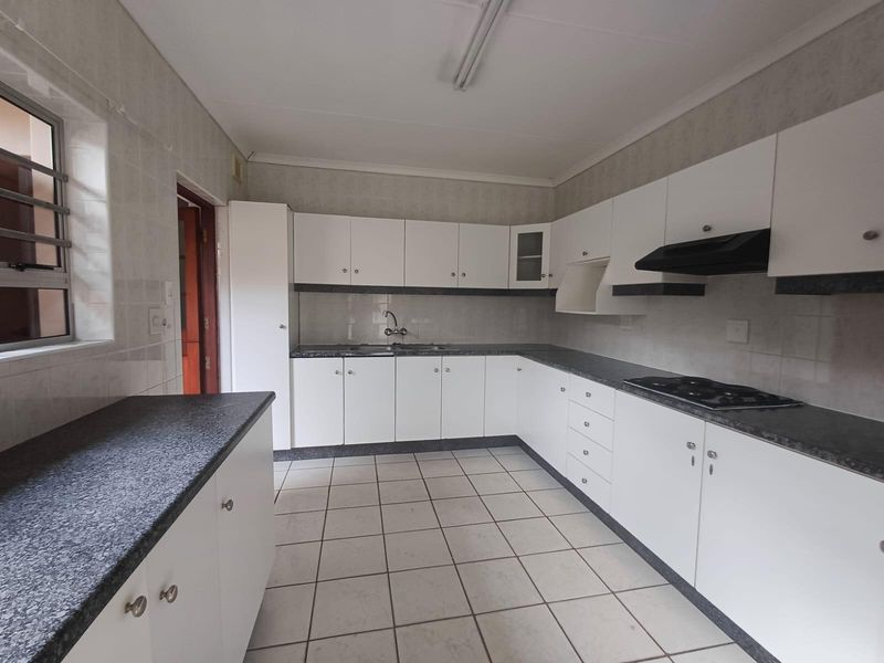 A functional, empty kitchen featuring white cabinetry, dark laminate countertops, a built-in hob with extractor fan, and neutral tiled flooring.