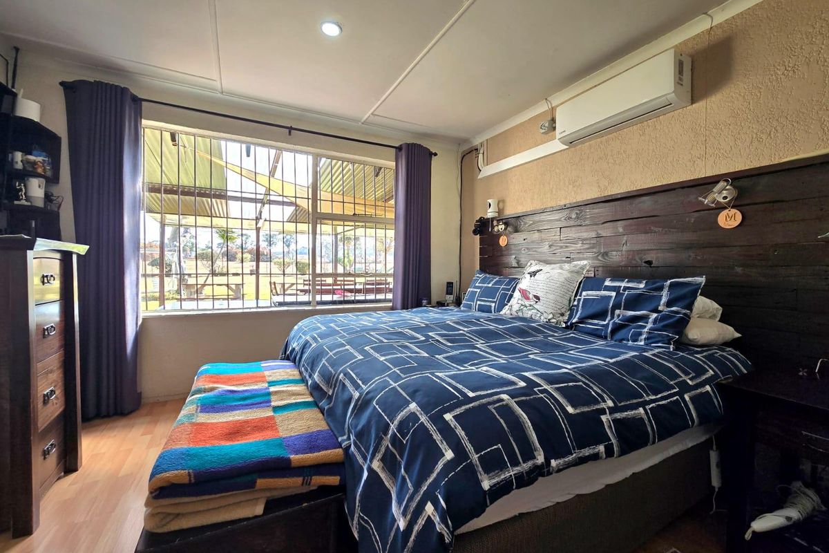 A bedroom featuring a timber headboard wall, laminate flooring, and a split-system air conditioner, with security bars installed on the window.