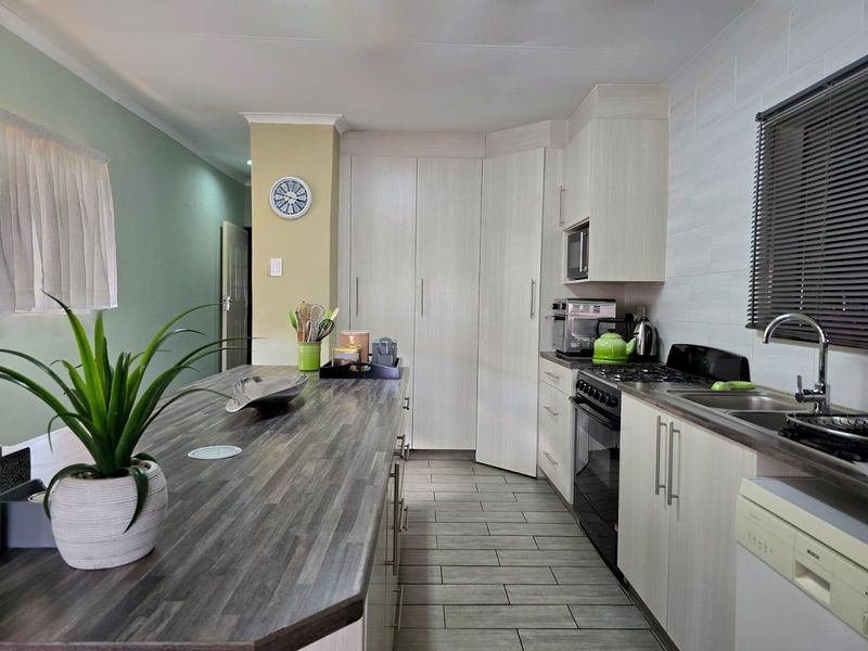 Modern kitchen featuring light wood-grain cabinetry, dark laminate countertops, a gas hob, built-in oven, and a functional breakfast bar island.