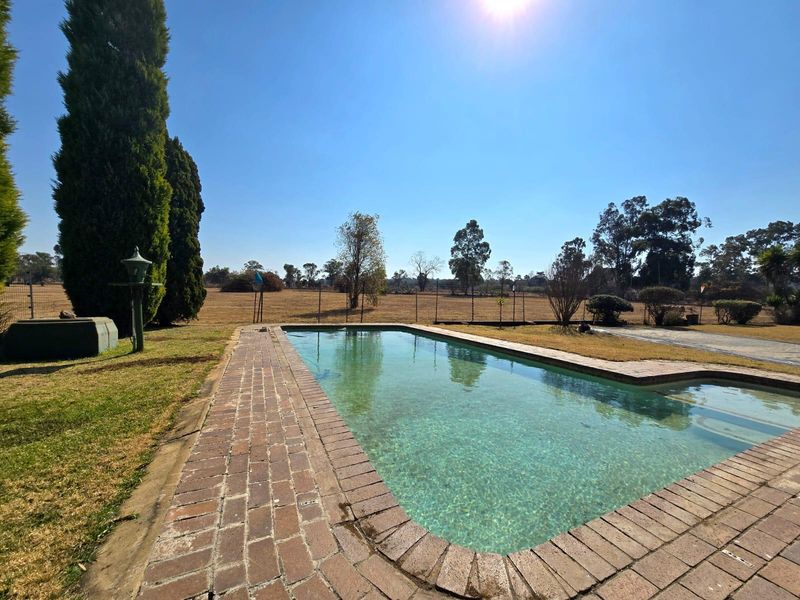 Outdoor swimming pool area featuring brick coping, surrounded by a lawn and wire fencing with open field views.