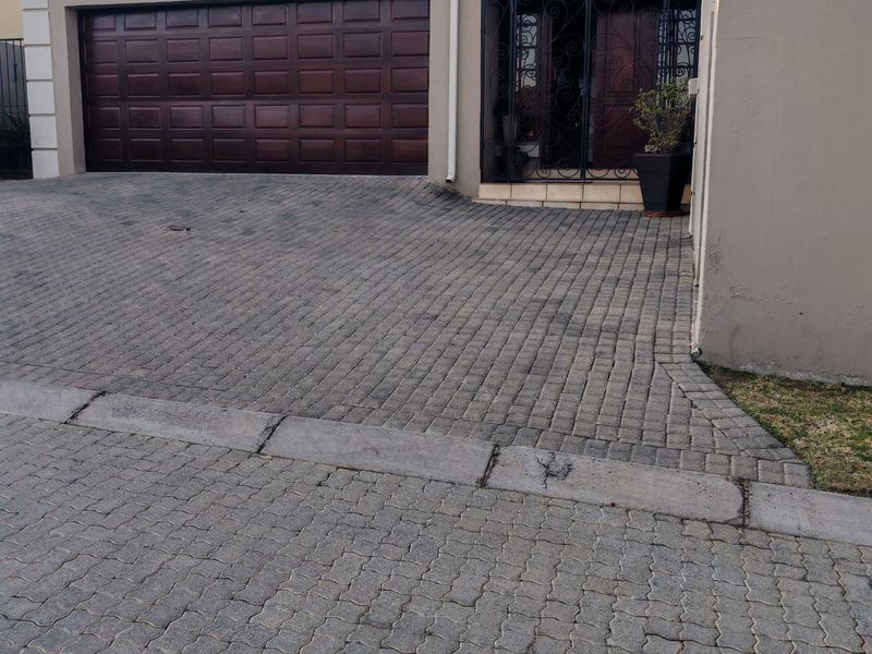 Front exterior view of the property featuring a paved driveway, double garage door, and a secure entrance with decorative metal security gate.