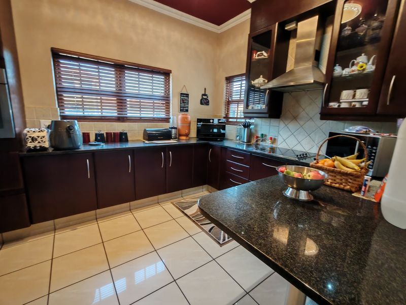 A functional kitchen featuring dark wood cabinetry, granite countertops, a stainless steel extractor fan, and tiled flooring with a neutral backsplash.