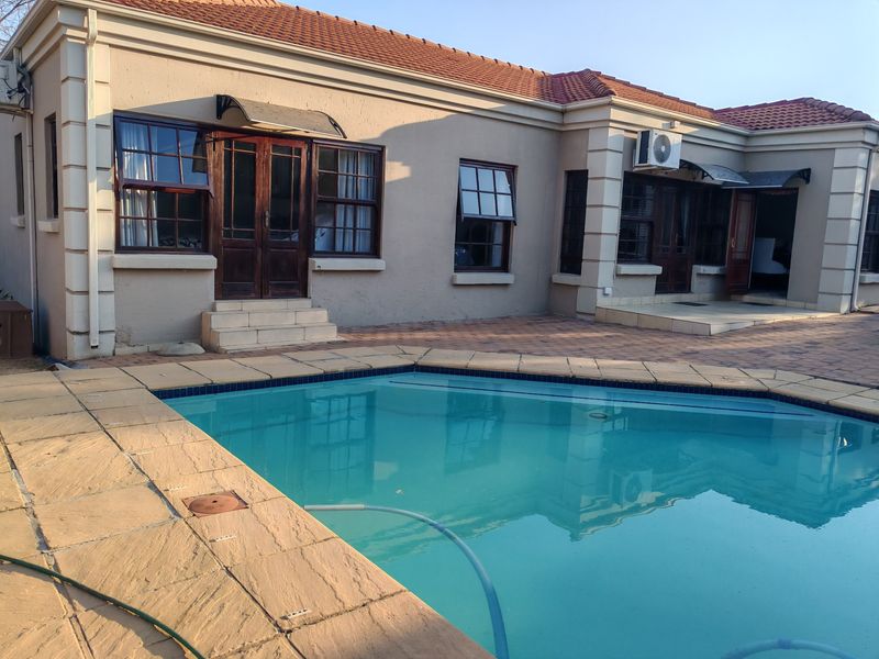 Rear exterior view featuring a swimming pool with paved surround, timber framed doors and windows, and a tiled roof.