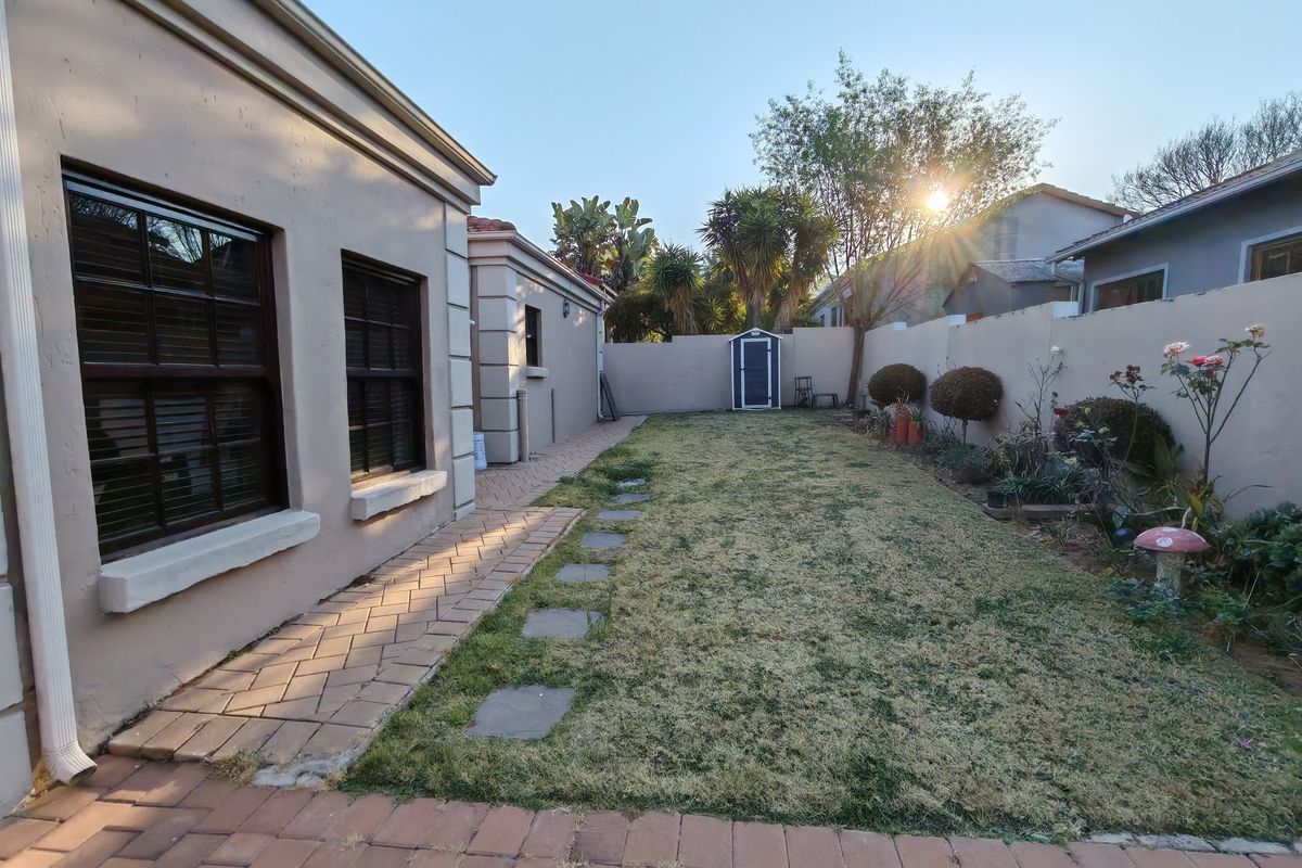 A private rear garden featuring a paved walkway, lawn area, and perimeter boundary walls with a small storage shed.
