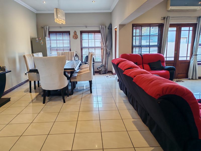 Spacious open-plan living and dining area featuring neutral tiled flooring, recessed lighting, and direct access to the exterior through timber-framed glass doors.