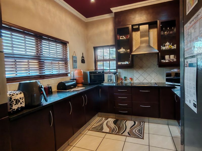 A functional kitchen featuring dark wood cabinetry, granite countertops, a stainless steel extractor fan, and tiled flooring with a distinctive deep red ceiling.