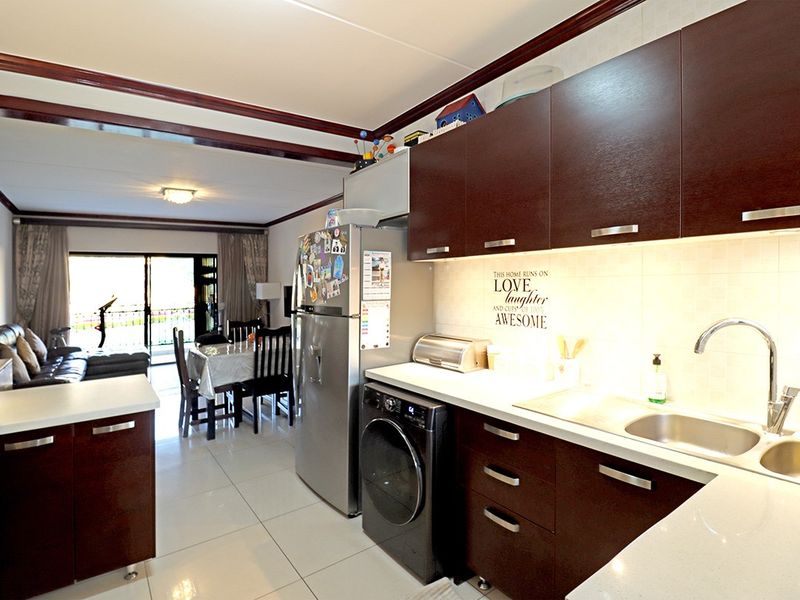 Open-plan kitchen and living area featuring dark wood cabinetry, stone countertops, and tiled flooring, creating a functional and connected living space.