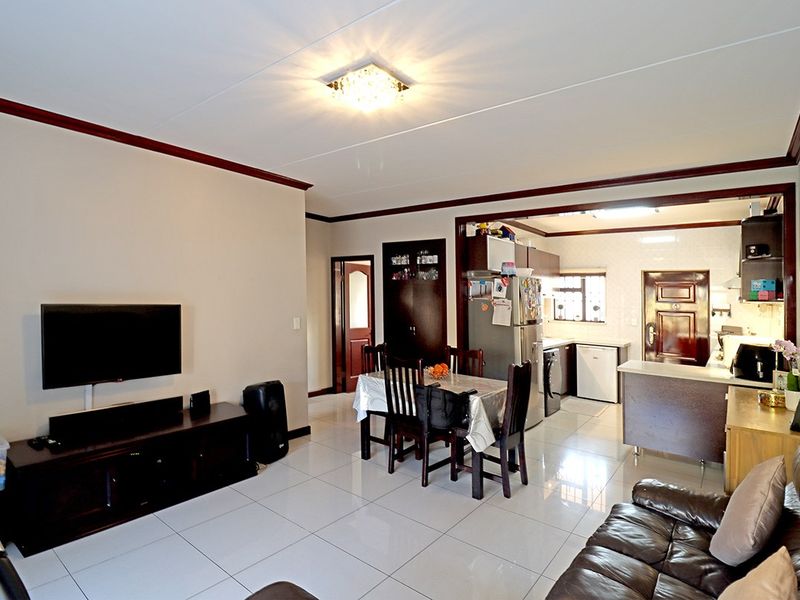 Open-plan living and dining area featuring tiled floors, flowing into a functional kitchen with built-in cabinetry and a breakfast counter.