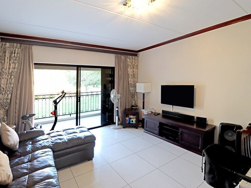 A living room featuring tiled flooring, crown molding, and a sliding glass door providing access to a balcony with a wrought iron railing.